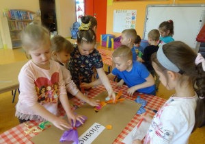 Dzieci przygotowują plakat, naklejają kolorowe kwiaty z bibuły.